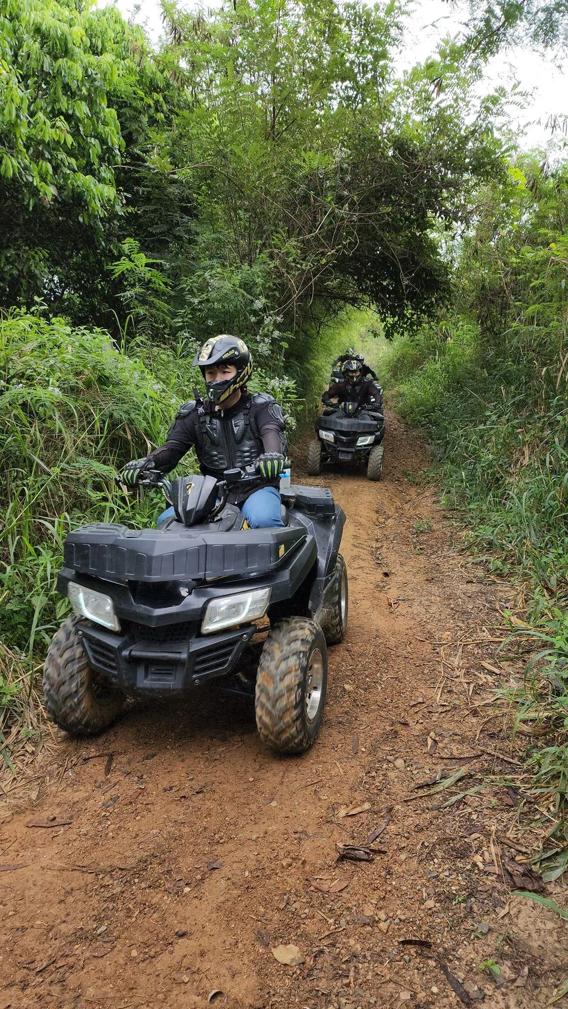 Picture of persons driving an ATV on a small dirt road in the jungle