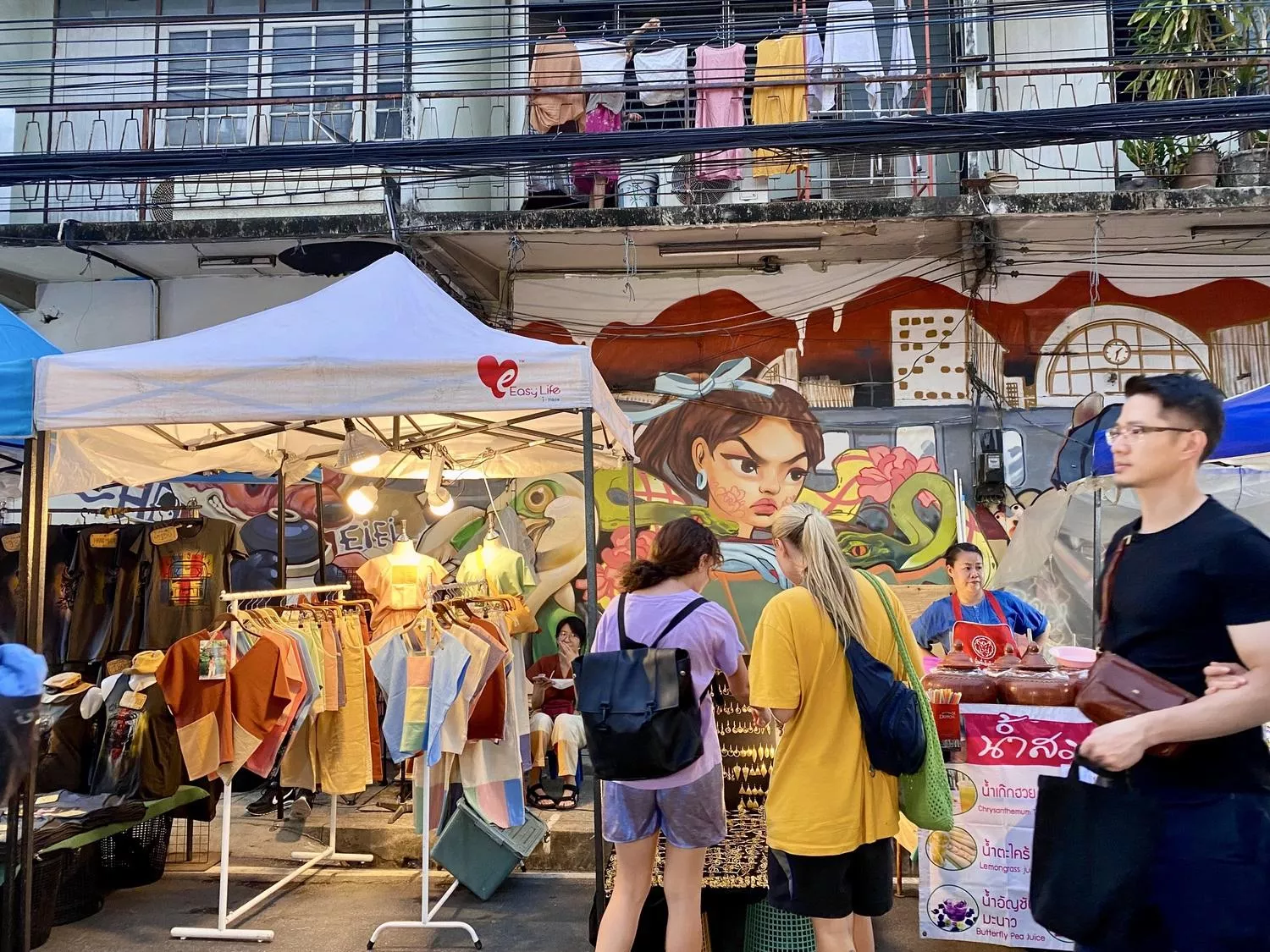 People and market stands with graffiti wallpainting in the background
