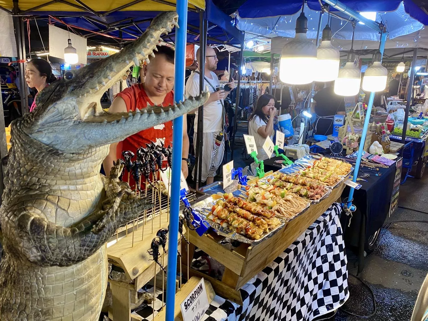 Small alligator statue next to barbecue food stand that sells alligator meat