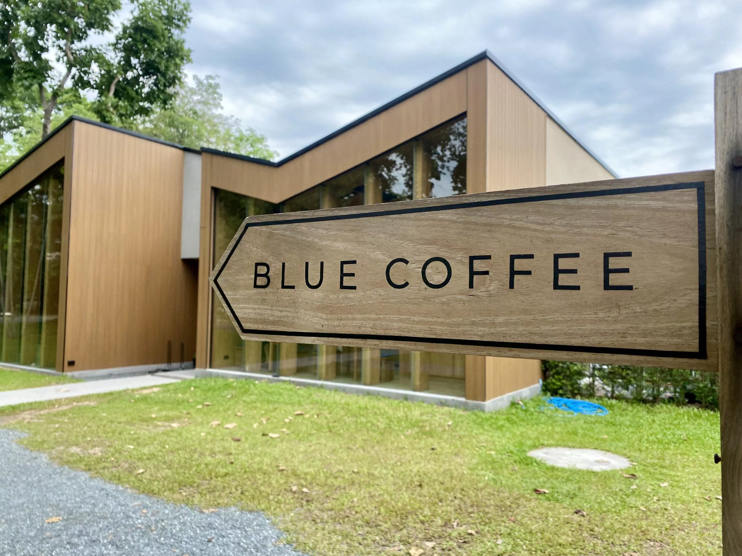 A wooden sign saying "Blue Coffee" and pointing towards the building behind it.