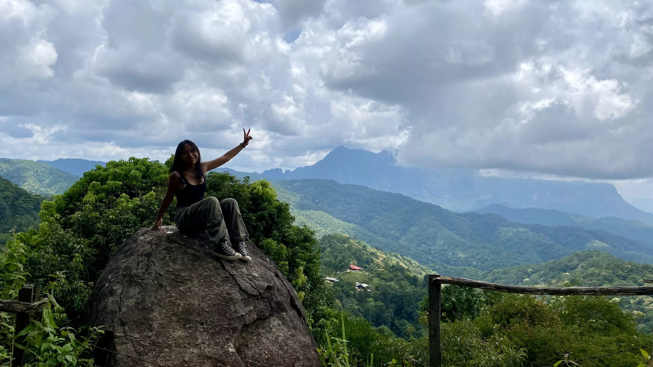 Lovely Thai girl sitting on a rock at a viewpoint over the mountain